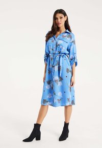 Blue floral dress made of satin with a belted waist, featuring short sleeves and a button-front design. Worn with black ankle boots.