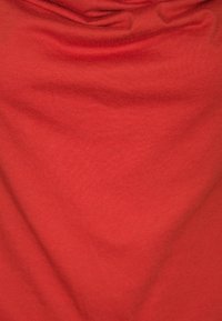 Czerwona bawełniana tkanina o gładkiej fakturze, z naturalnymi zagnieceniami i fałdami, tworząca luźny wygląd.