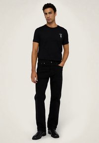 Svart bomulls-T-shirt med en liten grafik på vänster bröst, kombinerad med svarta jeans med raka ben och svarta ankelboots.