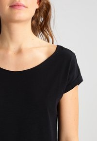 Svart kortärmad t-shirt med vid rund halsringning. Mjukt, lätt tyg med en slät yta, med upprullade ärmslut.