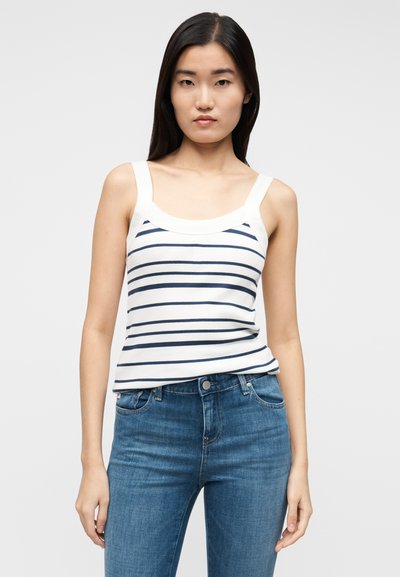 Ριγέ φανελάκι σε λευκό και σκούρο μπλε, κατασκευασμένο από ριμπ ύφασμα. Διαθέτει φαρδιές τιράντες και στρογγυλή λαιμόκοψη. Φορεμένο με μπλε τζιν.