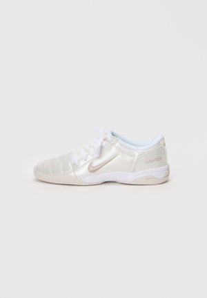 Fényes ezüstszínű sportcipők sima, fényes felsőrésze varrott panelekből készült, fehér fűzőkkel és bézs részletekkel a sarkon és a logón.