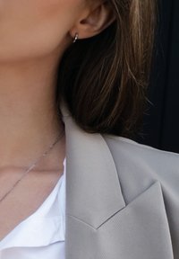 Sidabro auskaras su žiedu, pritvirtintas prie pradurtos ausies, su lygia, blizgia danga. Nešiojančiosios plaukai šviesiai rudi, dalinai matomi.