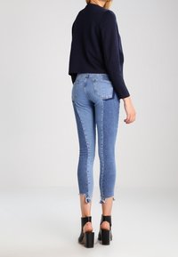 Pull court texturé bleu foncé porté avec un jean skinny bleu clair à ourlet brut, associé à des chaussures noires à talons carrés.