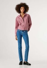 Rød- og hvitstripet skjorte med knappelukking og krage, kombinert med tettsittende blå jeans og svarte dressko. Enkel, klassisk passform og design.