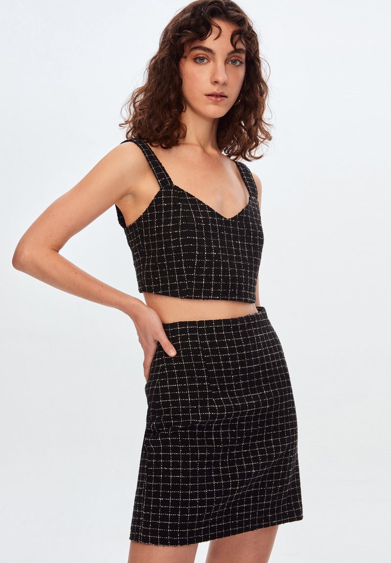 Conjunto de top corto y mini falda a cuadros en blanco y negro. La tela tiene un acabado texturizado, con una silueta estructurada y tirantes anchos.