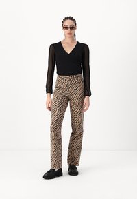 Svart innpakningsbluse med lange gjennomsiktige ermer, sammen med brune zebra-mønstrede bukser med vide ben. Kraftige svarte sko fullfører antrekket.