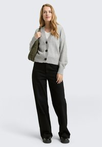 Cardigan gris tricoté avec cinq boutons noirs, porté par-dessus un haut blanc. Associé à un pantalon noir à jambes larges et un sac à épaule vert olive.