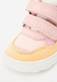 Sneaker per bambini con una tomaia in suede rosa, dettagli in suede giallo, suola in gomma bianca e cinturini in Velcro regolabili per la chiusura.