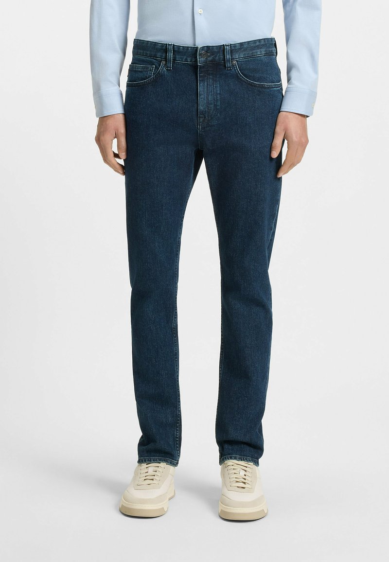 Mørkeblå denimjeans, slim fit, med frontlommer og beltehemper. Kombinert med lyse sneakers, glatt tekstur.