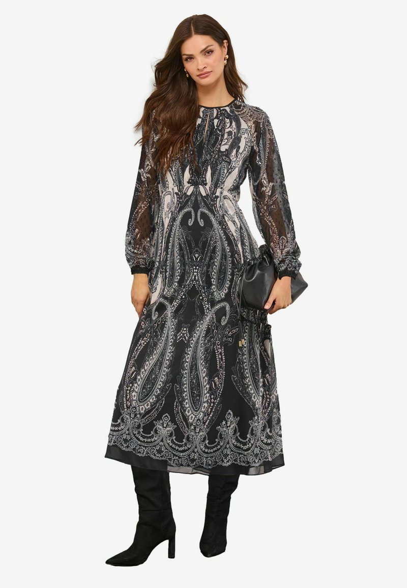 Rochie lungă neagră cu model paisley, mâneci transparente, modele albe și gri detaliate, talie strânsă și fustă vaporoasă. Asortată cu încălțăminte neagră.