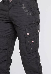 Pantalons cargo noirs avec plusieurs poches, accents de bouton et détails brodés. Fabriqués en tissu texturé, présentant une coupe fuselée.