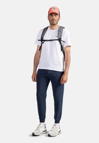 Šedý batoh se straps, bílý tričko, námořnické kalhoty a bílé tenisky. Čepice zdobí grafika hory v oranžové a červené barvě.