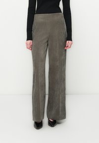 Cordial wide-leg trousers in olive green corduroy, featuring vertical ridges, a high waist, and a soft texture. Pair with black shoes.