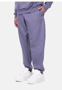 Purple sweatpants with a relaxed fit, elastic cuffs, and side pockets. Paired with white sneakers showcasing a textured surface.