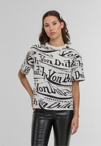 Balta marškinėliai su juodais "Von Dutch Originals" logotipais, trumpomis rankovėmis, apvaliu kaklu, laisvuoju siluetu, derinami su juodomis aptemptomis džinsomis.