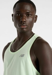 Light green athletic tank top made of breathable material, featuring a small silver logo and a textured, perforated design.