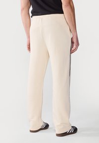 Beige sweatpants med en afslappet pasform, der har sorte sidelommer, en elastisk talje og blødt bomuldsstof.