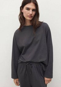 Tmavě šedý dlouhý rukáv s měkkého materiálu, doplněný o odpovídající kalhoty na stažení, s volným střihem a minimalistickým designem.