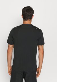 Camiseta atlética negra de manga corta con un cuello redondeado y pequeños acentos blancos en los hombros, hecha de una tela suave y ligera.