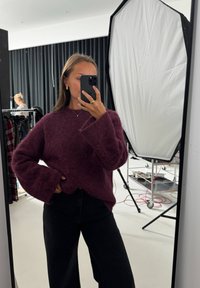 Vibrant burgundy tröja med en fluffig textur, vida ärmar och en lätt fåll, tillsammans med hög midja svarta texturerade byxor.