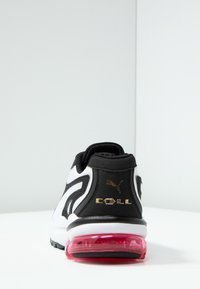 Baskets noir et blanc avec une tige texturée, un col rembourré et un coussin d'air rose transparent au talon. Présente un détail de logo doré.