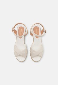 Beige cross-strap sandals with a woven jute sole and adjustable ankle strap, featuring a smooth fabric and a light tan insole with branding.