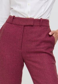 Weinrote Hosen mit Fischgrätenmuster, tailliert, mit Seitentaschen und Gürtelschlaufen, gefertigt aus strukturiertem Stoff.