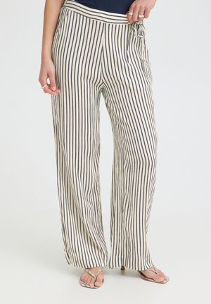 Personne portant un pantalon taille haute à jambes larges avec des rayures verticales noires et blanches, noué à la taille, associé à des sandales à talons ouvertes.