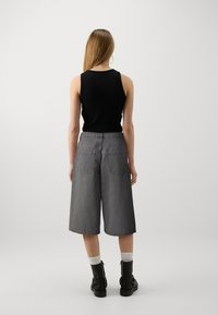 Top negro sin mangas combinado con culottes de mezclilla gris de pierna ancha y cintura alta. El conjunto presenta bolsillos traseros y un ajuste relajado.