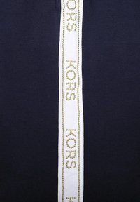 Námořnická látka s vertikálním bílým pruhem, na kterém je zlatým korálkovým písmem nápis "KORS". Hladká textura s čistým, moderním designem.