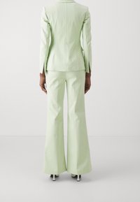 Completo verde chiaro composto da un blazer su misura con silhouette aderente e pantaloni svasati. Tessuto liscio con maniche lunghe e spacchi posteriori.