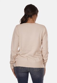 Maglione beige a maniche lunghe con scollo rotondo e orlo a coste. Tessuto morbido e testurizzato con vestibilità comoda, mostrato da dietro.