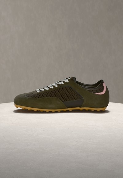 Σκούρο πράσινο αθλητικό παπούτσι casual με πλευρές από δίχτυ, λευκά κορδόνια, σόλα χρώματος καουτσούκ και ροζ χρωματισμό στη φτέρνα, τοποθετημένο σε ανοιχτόχρωμη επιφάνεια με υφή.