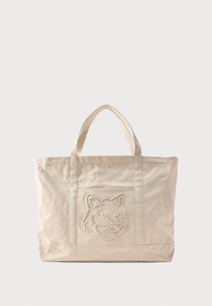Beige canvas tote bag with double handles and an embossed wolf head design on the front pocket.