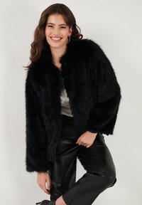 Black faux fur jacket with a relaxed fit, long sleeves, and a soft texture, paired with black leather pants and a light top.