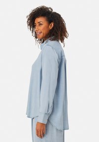 Camicia azzurra chiara a maniche lunghe realizzata in tessuto morbido. Presenta un colletto a punta, polsini con bottoni e un orlo curvo per un fit rilassato.