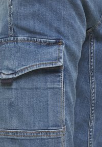 Pantalones cargo de denim en azul claro con un acabado texturizado, que cuentan con un bolsillo lateral y costuras dobles a lo largo de las costuras para mayor durabilidad.