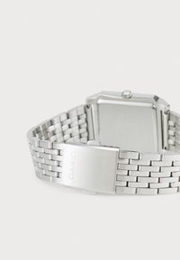 La montre Casio argentée présente un cadran rectangulaire, un bracelet en acier inoxydable avec des maillons tissés, et une boucle en métal brossé.