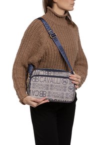 Borsa a tracolla blu e beige con motivo logo, chiusura con zip e tracolla regolabile. Realizzata in tessuto resistente con una texture liscia.