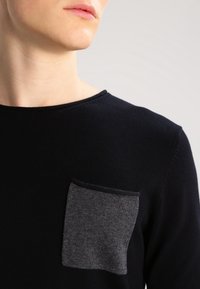 Marinblå tröja med rund halsringning och en framträdande grå fickdetalj, med en slät textur och figurnära design.