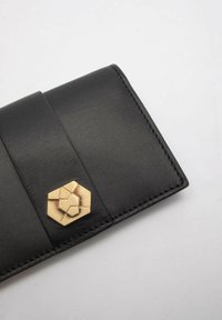 Čierna kožená peňaženka s textúrovaným povrchom, hexagonálnym zlatým akcentom a prešívanými okrajmi. Dizajn zahŕňa elegantný, minimalistický štýl.