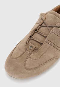 Chaussure en suède brun avec un bout rond, dotée d'accents de couture, d'un système de laçage fermé et d'un petit détail de logo métallique.