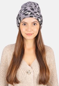 Graue Strickmütze mit schwarz-weißer Leopardenmusterung. Weiches, strukturiertes Material mit fester Passform. Kombiniert mit einem hellbeigen gestrickten Cardigan.