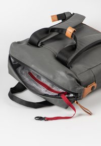 Grijze rugzak van glad materiaal, met zwarte schouderbanden, bruine leren accenten en een rode rits voor het interieurvak.