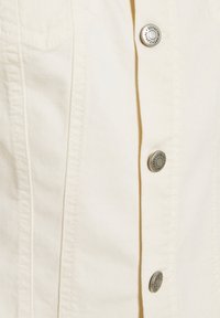 Giacca di jeans leggera crema con chiusura a bottoni, dotata di accessori in argento, due tasche sul petto e dettagli di cucitura a contrasto.
