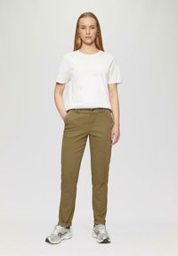 Weißes Baumwoll-T-Shirt, kombiniert mit olivgrünen, schmal zulaufenden Hosen, die vordere Taschen und einen Knopfverschluss aufweisen, ergänzt durch silberne Sportschuhe.