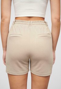 Bermuda beige con una vita elasticizzata, due tasche posteriori, superficie liscia e silhouette aderente, viste da dietro.