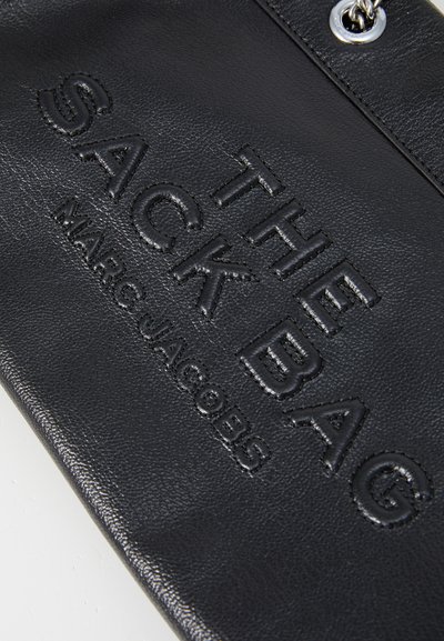 Crna kožna torba u obliku vreće s uklesanim natpisima "THE SACK BAG" i "MARC JACOBS"; ukrašena srebrnim hardverom za moderni izgled.