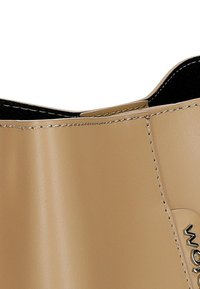 Bottine beige brillante avec une surface lisse, une légère courbure sur le haut et des détails de couture visibles le long du bord.